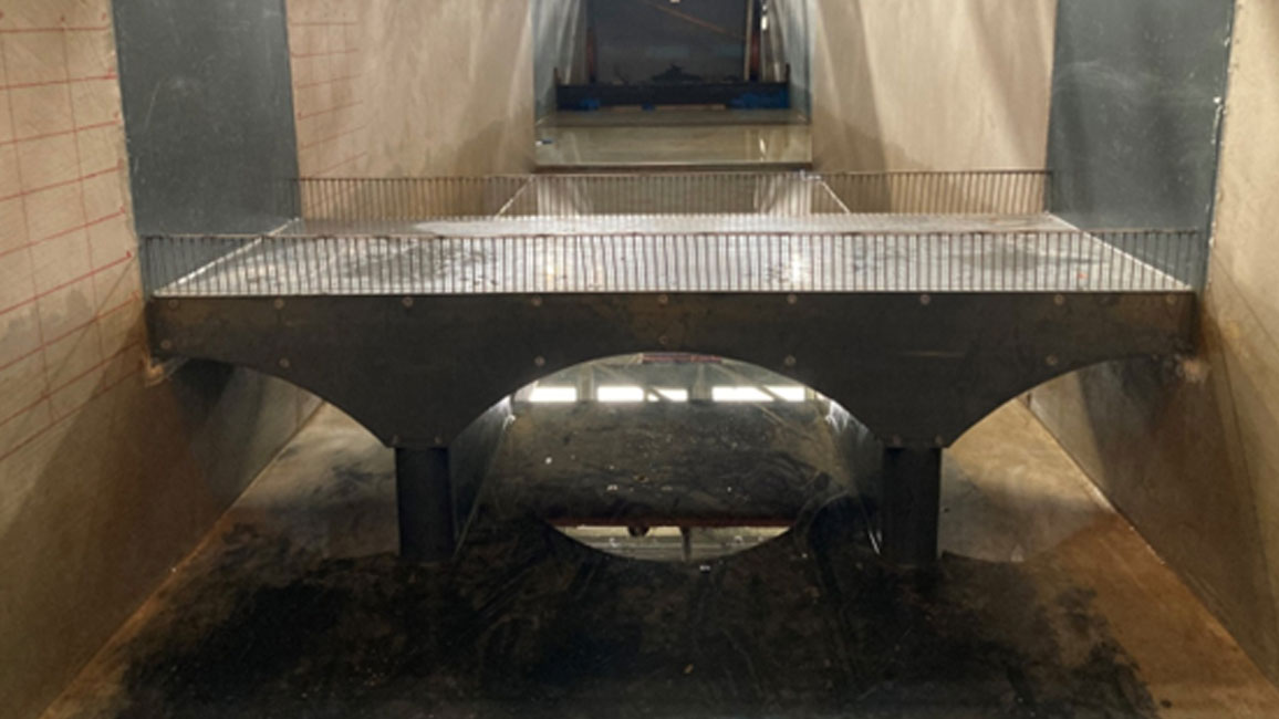 Strömungskanal in der Versuchshalle des Instituts für Wasserbau und Wasserwirtschaft der RWTH Aachen mit Brückenmodell und Wasserfluss unter der Brücke.